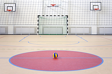 A school sports hall with a marked indoor football pitch, goal and basketball hoops, a striped blue and yellow ball in a pink circle.