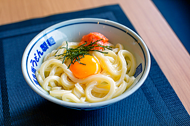 A dish of noodles, vegetables and fish with a yellow egg yolk.