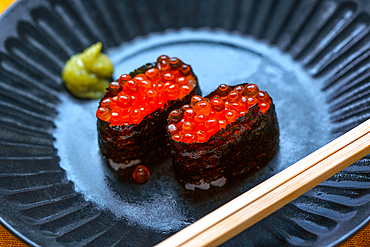 A dish with two portions of sushi, rice wrapped in seaweed with fish roe.