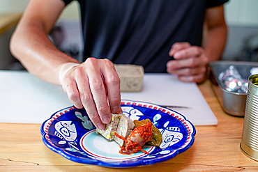 A man preparing food in a restaurant, placing vegetables and pate on a plate. Close up.