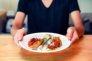 A man standing at a restaurant counter presenting plates of cooked food, menu dishes.