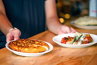 A man standing at a restaurant counter presenting plates of cooked food, menu dishes.