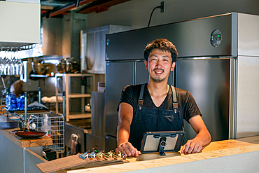 A man standing at the counter of a restaurant kitchen, using a digital tablet, the owner or manager.