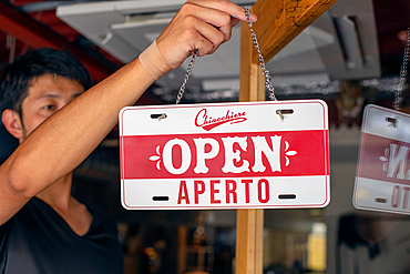 Man hanging up an Open sign on a restaurant door. - Dual language, Italian and English.