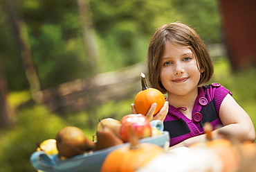 A young girl holding a pumpkin in her hand at a table outside. Harvest time, Woodstock, New York, USA