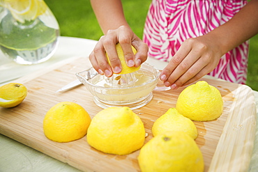 A summer family gathering at a farm. A girl slicing and juicing lemons to make lemonade.