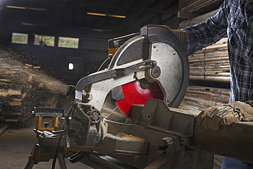 A reclaimed lumber workshop. A man in protective eye goggles using a circular saw to cut timber, Woodstock, New York, USA