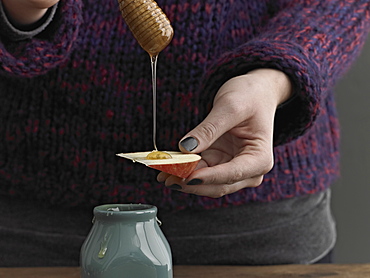 A woman drizzling honey from a round wooden drizzle stick on to an apple slice, New York city, USA