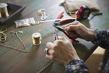 A tabletop with jewellery making equipment. Hands twisting wire on a necklace, New York, USA