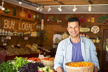 A farm growing and selling organic vegetables and fruit. A man holding a bowl of basket of freshly picked tomatoes, Hurley, New York, USA