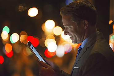 A man in a city at night, looking at a computer tablet, New York city, USA