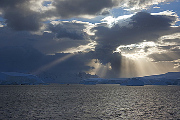 Sun breaking through the storm clouds hitting the icebergs along the west coast of the Antarctic Peninsula, Antarctica