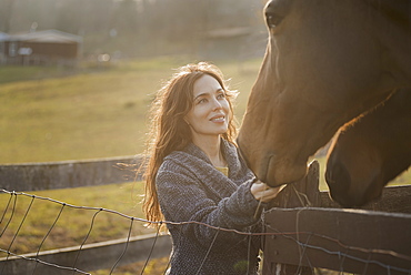 A woman stroking the muzzles of two horses in a paddock on an organic farm, Saugerties, New York, USA