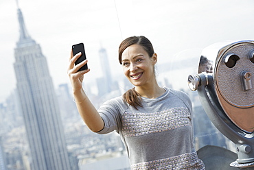 New York City. An observation deck overlooking the Empire State Building. A woman using her smart phone to take a photograph of herself and the view over the city, New York city, USA