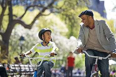 A family in the park on a sunny day. Bicycling and having fun. A father and son side by side.