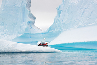 People in small inflatible zodiac rib boats passing towering sculpted icebergs on the calm water around small islands of the Antarctic Peninsula, Antarctic Peninsula, Antarctica