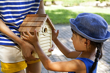 Young girl wearing a summer dress and sun hat, holding a bird house, Kyoto, Honshu Island, Japan