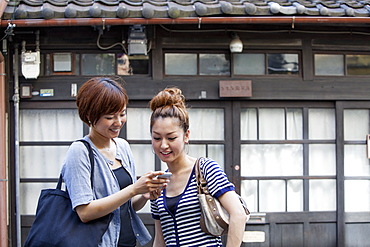 Two women standing outdoors, looking at cellphone, Osaka, Japan