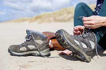 Young woman taking her hiking boots off on the beach at Harlech, Gwynedd, Wales