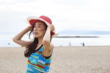 A woman on a beach in Kobe holding her hat on, Kobe, Japan