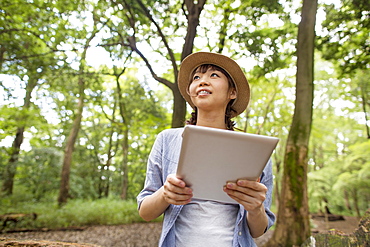 Young woman holding a digital tablet in a forest, Kyoto, Japan