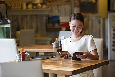 Woman sitting at a table in a cafe, holding the bill and her purse, smiling, Osaka, Japan