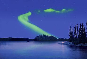 The Northern Lights in the night sky, the Aurora borealis above a calm lake, Two people by a fire on the lake shore, Canada