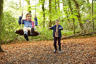 Beech woods in Autumn. A girl sitting on a swing being pushed by her brother, England, United Kingdom