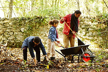 A family raking and scooping up leaves in autumn, England, United Kingdom