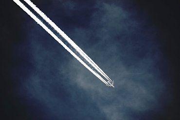 A jet with a clear condensation or vapour trail or contrail across a dark blue sky