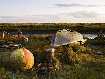 An upturned fishing boat by a narrow water channel in a flat landscape. Fishing floats and buoys, Fishing boat, England