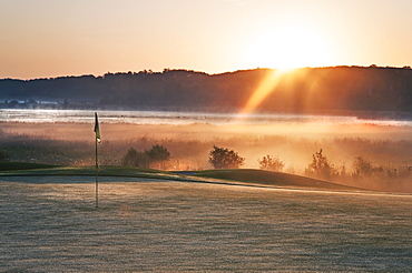 Glowing dawn light on a golf course green. The sun just appearing above a mountain range, Kenosee, Saskatchewan, Canada