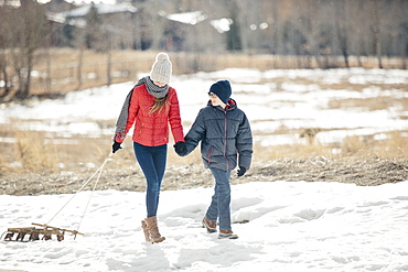 A brother and sister in the snow, one pulling a sledge, Mountains, Utah, USA