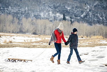 A brother and sister in the snow, one pulling a sledge, Mountains, Utah, USA