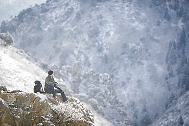 A man, a hiker in the mountains, taking a rest on a rock outcrop above a valley, Mountains, Utah, USA