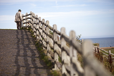 An elderly man standing on the seafront walkway looking out to sea, Sea coast, Northumberland, England