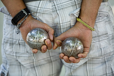 A boules player with one metal ball in each hand, held behind his back, Boules player, France