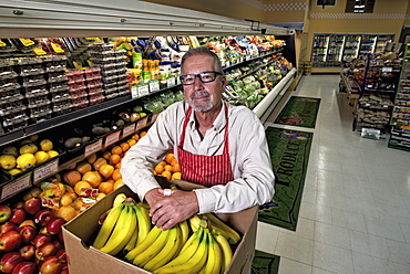 A man standing in a grocery shop beside a display of fresh fruits and vegetables.