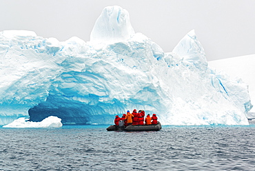 Group of people crossing the ocean in the Antarctic in a rubber boat, icebergs in the background.