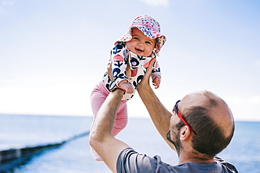 A father lifting his baby daughter in a sun bonnet up in the air, , England