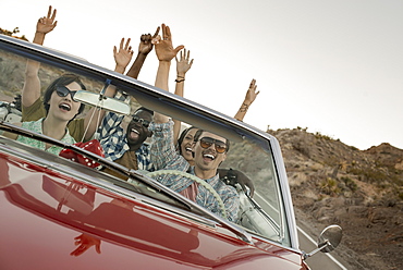 A group of friends in a red open top convertible classic car on a road trip, United States of America