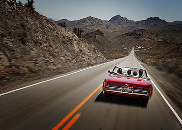 A red convertible car with five young people on a road trip. The open road, United States of America