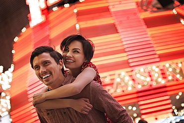 A man giving a woman a piggyback, under a bright neon Casino sign, United States of America