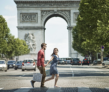 A couple hand in hand carrying shopping bags and crossing the road by a historic monument in the heart of a European city, France