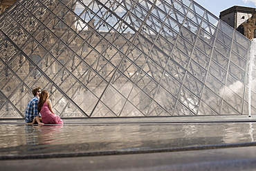 A couple in the courtyard of the Louvre museum, by the large glass pyramid. Fountains and water, France