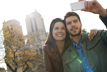 A man holding a smart phone taking a selfy of himself and his girlfriend in front of Notre Dame cathedral, France