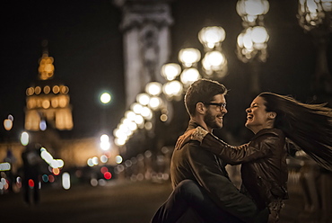 A couple close together facing each other, embracing in a city at night, France