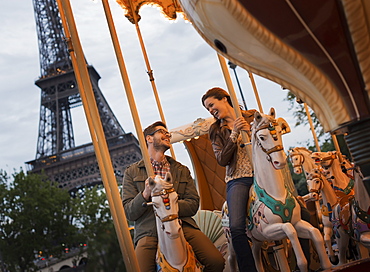 A couple, man and woman riding traditional gallopers on a carousel ride in the shadow of the Eiffel Tower in Paris, France