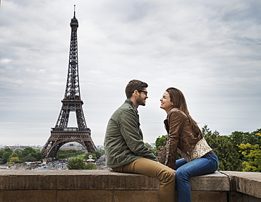 A couple seated facing each other on a wall in the city of Paris with the Eiffel Tower in the background, France