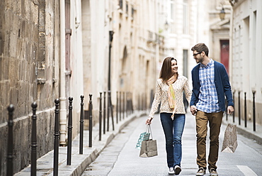 A couple walking along a narrow city street with shopping bags, France